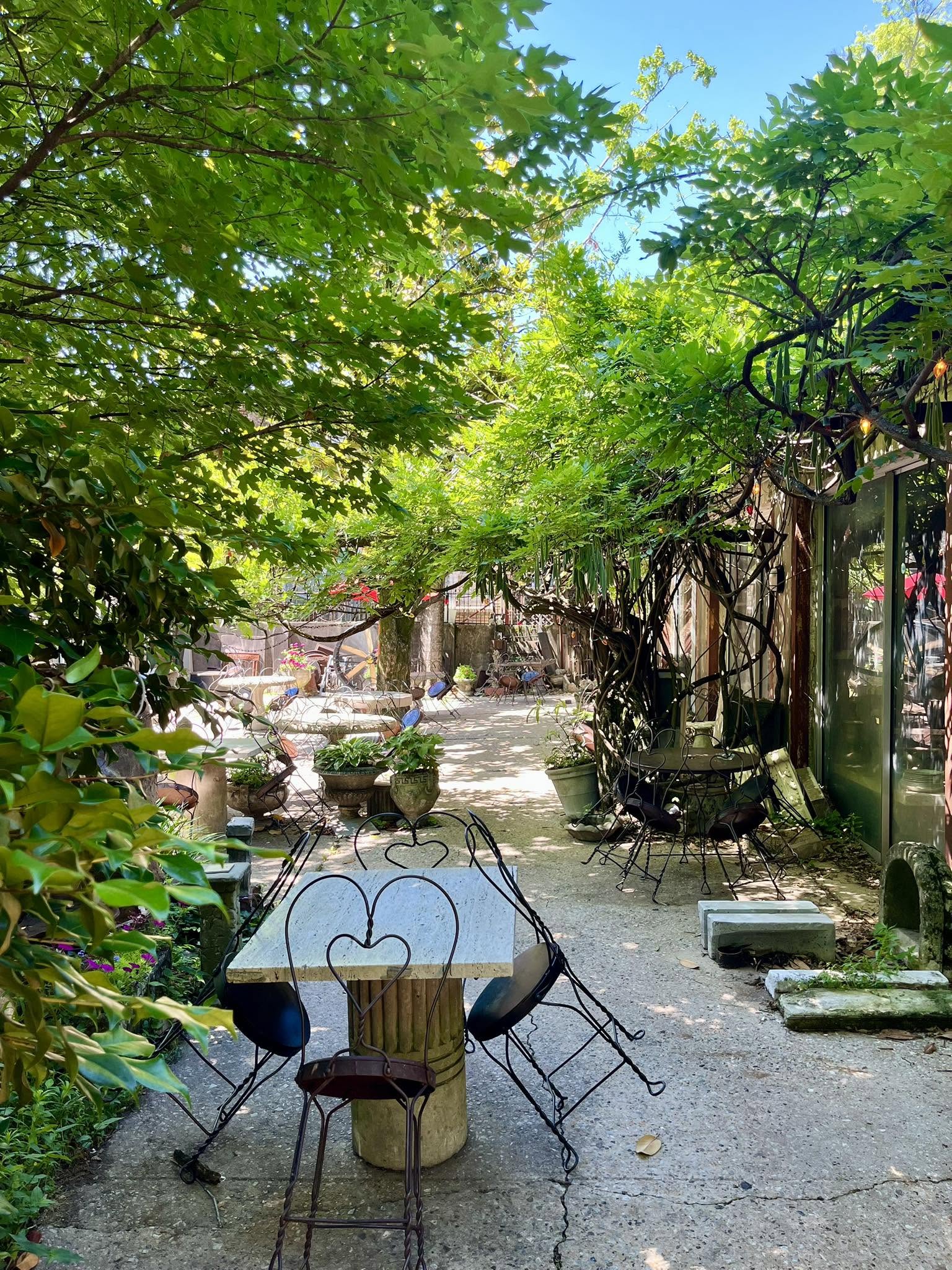 Heart-back wire chairs and a table in a shaded corner of the courtyard