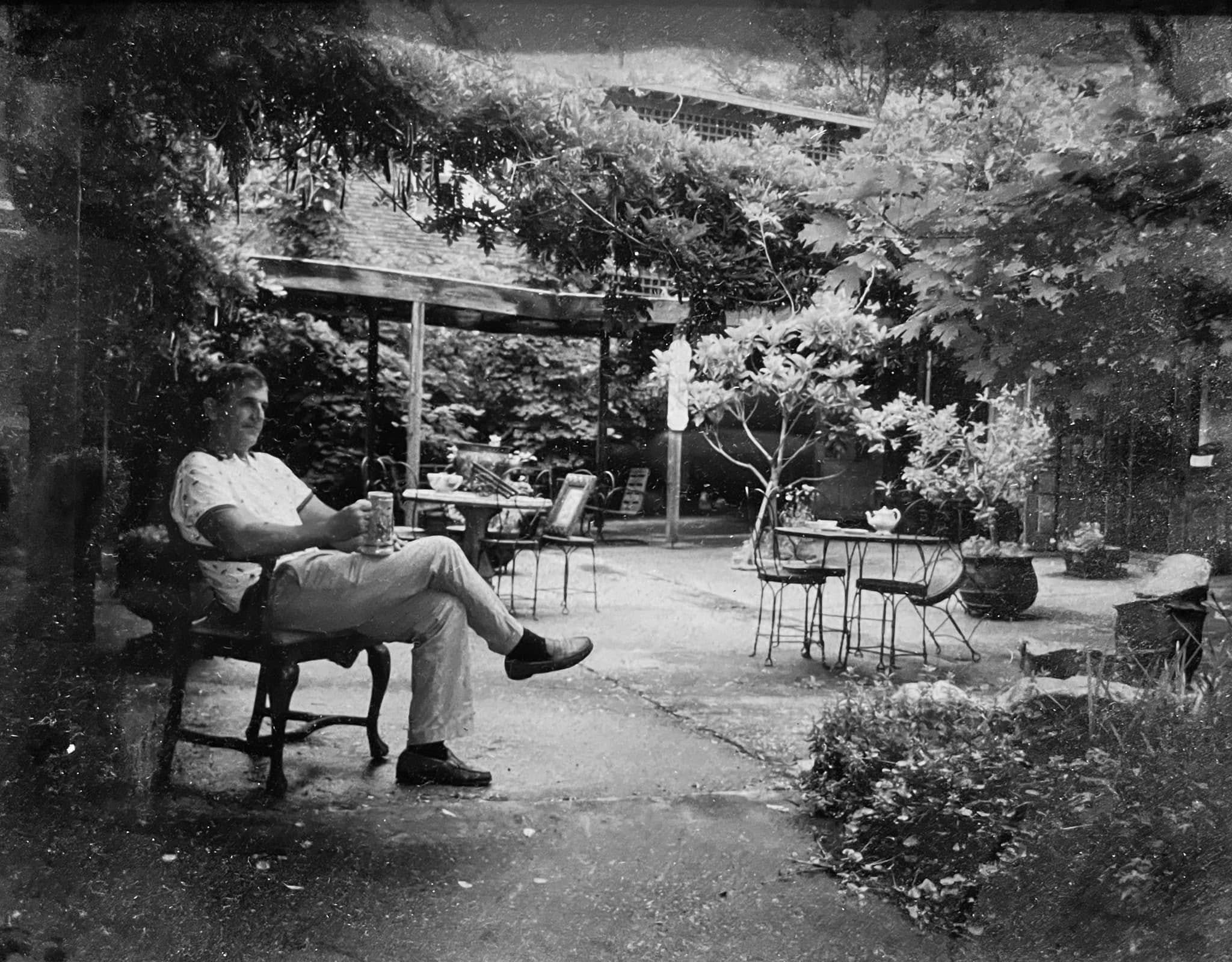 Black and white photo of a man relaxing with a drink in the courtyard, an early look at the space